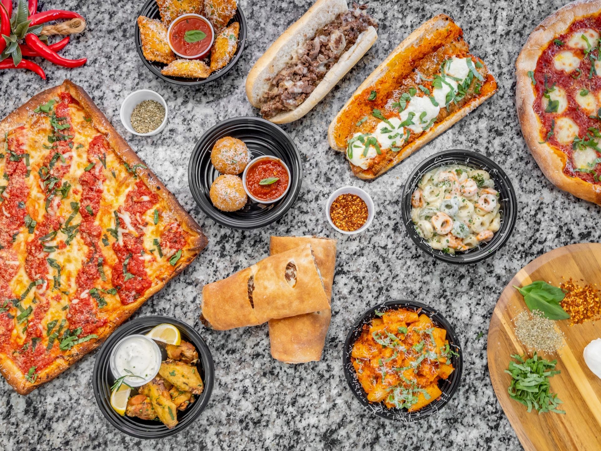 Enzo's pizza, arancini, calzones and pasta spread on a marble counter